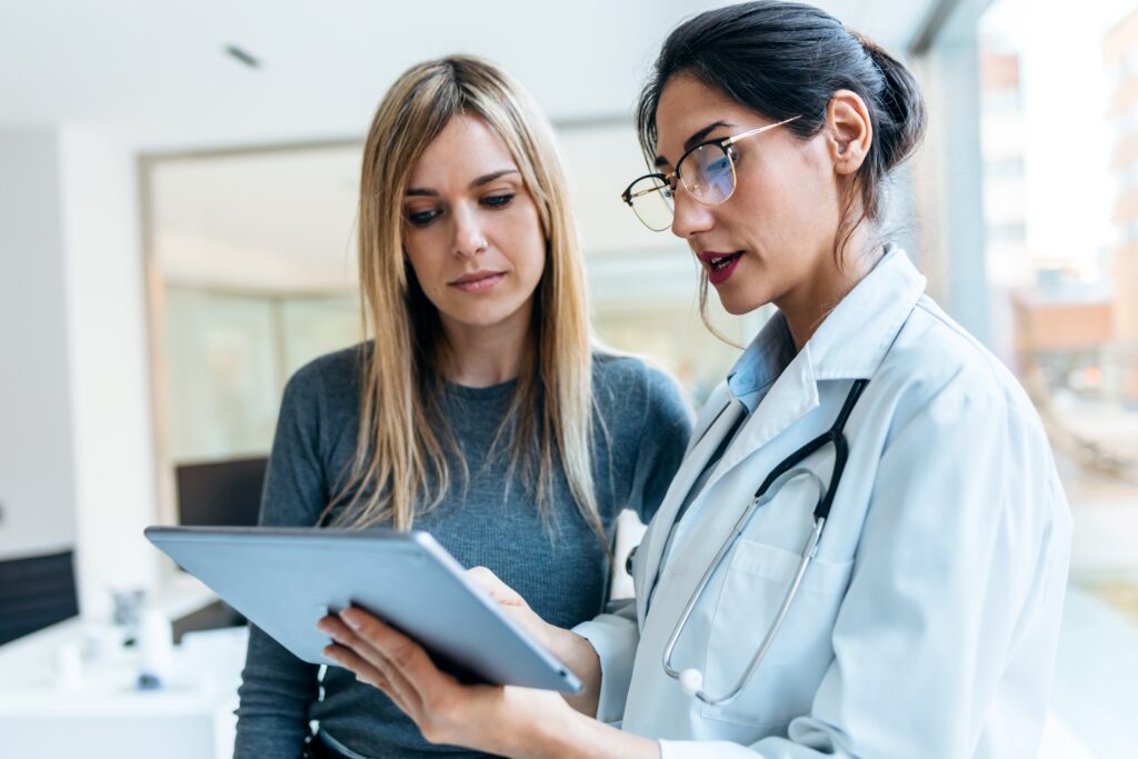 Doctora muestra información en tableta a paciente, abordando detalles de atención y posibles costos médicos durante la consulta.