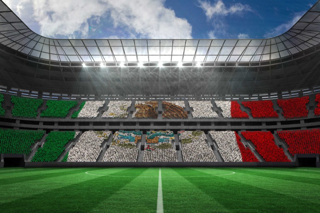 Vista interior de un estadio de fútbol lleno de aficionados formando la bandera de México en las gradas, bajo un cielo parcialmente nublado.