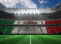 Vista interior de un estadio de fútbol lleno de aficionados formando la bandera de México en las gradas, bajo un cielo parcialmente nublado.