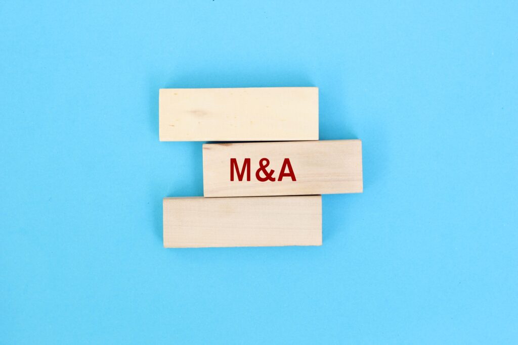 Concepto visual de fusiones y adquisiciones representado con bloques de madera y las siglas M&A, en referencia a la estrategia de crecimiento de TWFG Insurance.