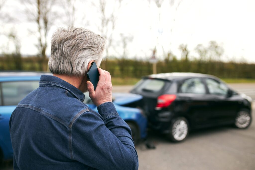 Hombre mayor llama por teléfono tras un choque entre dos autos, ilustrando la importancia del seguro de automóvil y la cobertura Green Card en caso de siniestro.