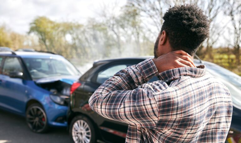 Hombre lesionado sostiene su cuello tras un choque automovilístico, reflejando cómo las quejas crecen contra aseguradoras de auto en Michigan por rechazar pagos con pretextos.