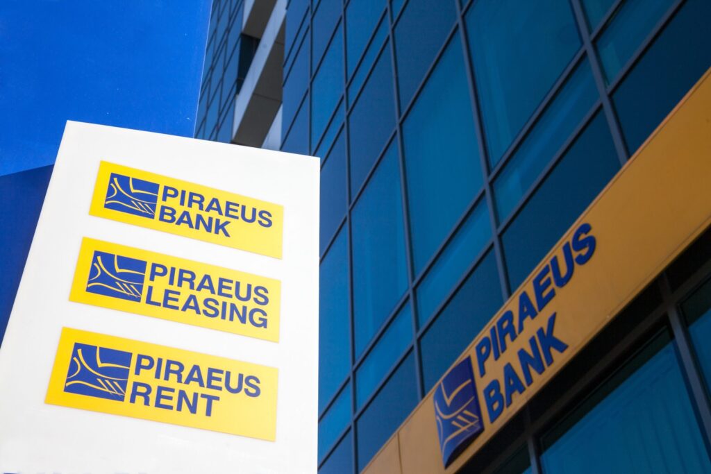 Logotipo de Piraeus Bank en edificio corporativo en Grecia, ilustrando la adquisición de Ethniki Insurance autorizada por la Comisión Helénica de Competencia.