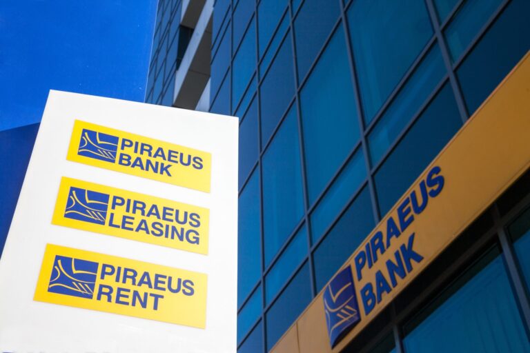 Logotipo de Piraeus Bank en edificio corporativo en Grecia, ilustrando la adquisición de Ethniki Insurance autorizada por la Comisión Helénica de Competencia.