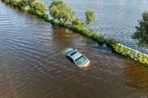 Automóvil parcialmente sumergido en agua tras una inundación en zona urbana, reflejando el impacto de fenómenos hidrometeorológicos en bienes no asegurados.