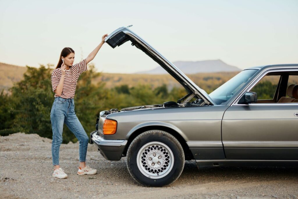 Mujer preocupada revisando un auto viejo descompuesto, reflejo del impacto de los autos viejos en el costo del seguro en Argentina.