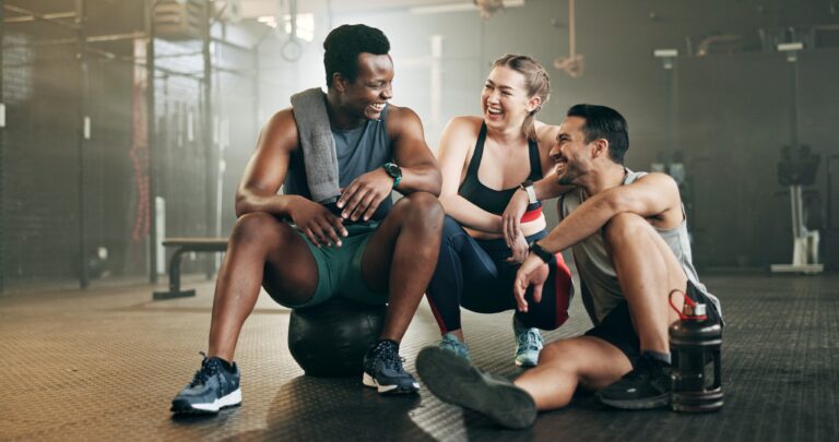 Grupo de jóvenes en gimnasio sonríe tras entrenar, ilustrando beneficios ocultos de los seguros médicos como pases de gimnasio y programas de bienestar