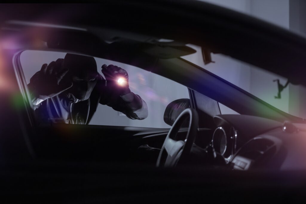 Hombre intentando robar un automóvil visto desde el interior, ilustrando la importancia de los seguros vehículo frente a delitos y riesgos urbanos.