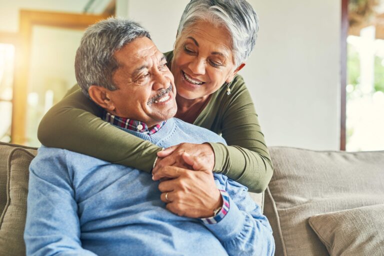 Pareja de adultos mayores sonríe en casa, representando seguridad financiera y estabilidad económica gracias a un seguro de vida.