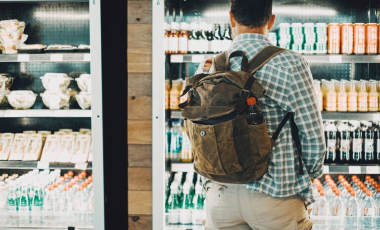 Hombre frente a un refrigerador con refrescos y aguas embotelladas, ilustrando cómo la regulación influye en la oferta y elección del consumidor.