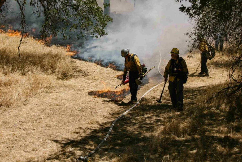 Cuerpo de bomberos actuando ante incendio junto a documentos de seguro, reflejando la obligación de aseguradoras paguen bomberos.