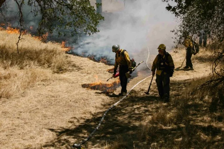Cuerpo de bomberos actuando ante incendio junto a documentos de seguro, reflejando la obligación de aseguradoras paguen bomberos.